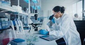 A researcher looks through a microscope in a pharmaceutical lab